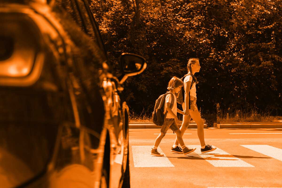 Children crossing the street at a crosswalk during sunset with a car nearby.