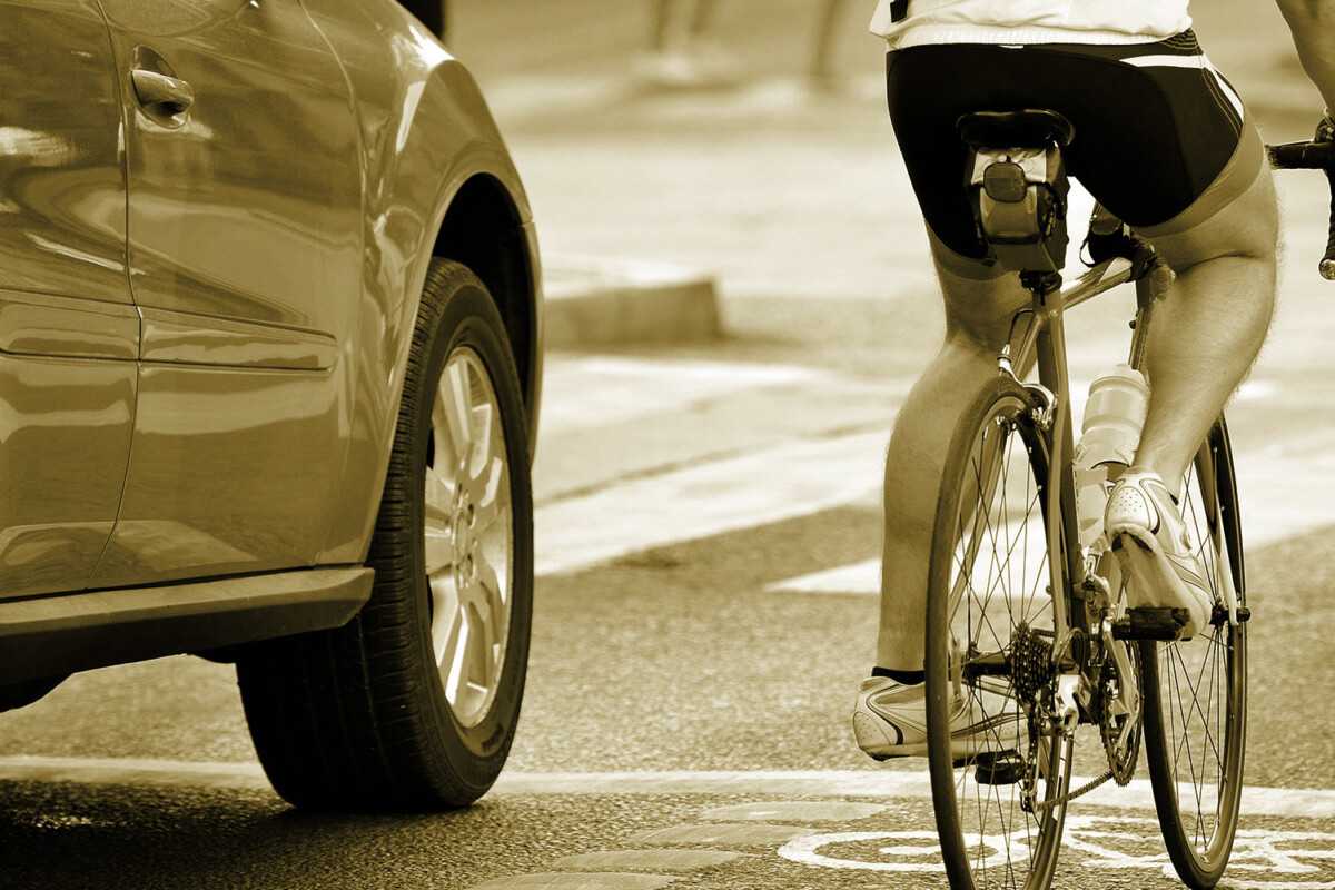Cyclist riding near parked car on city street in sepia tone.