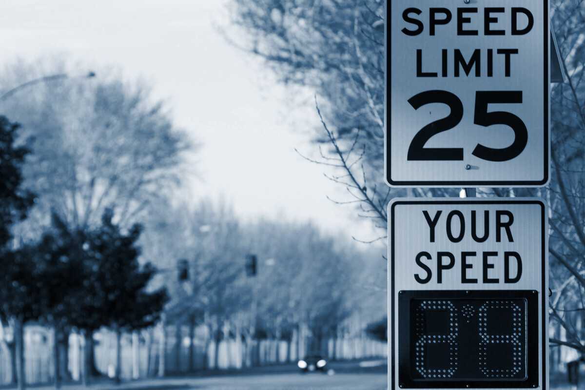 Speed limit sign and digital speed display on a road in winter.