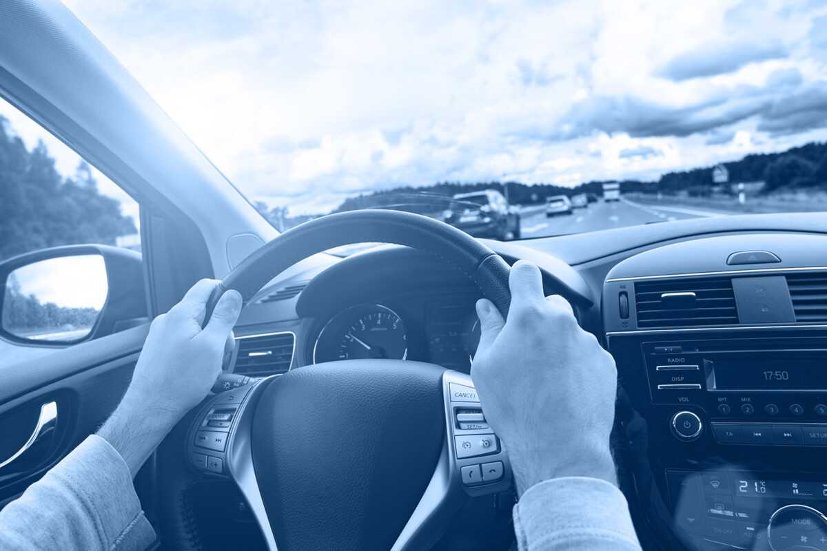 Driver holding steering wheel on a highway with cars and cloudy sky.