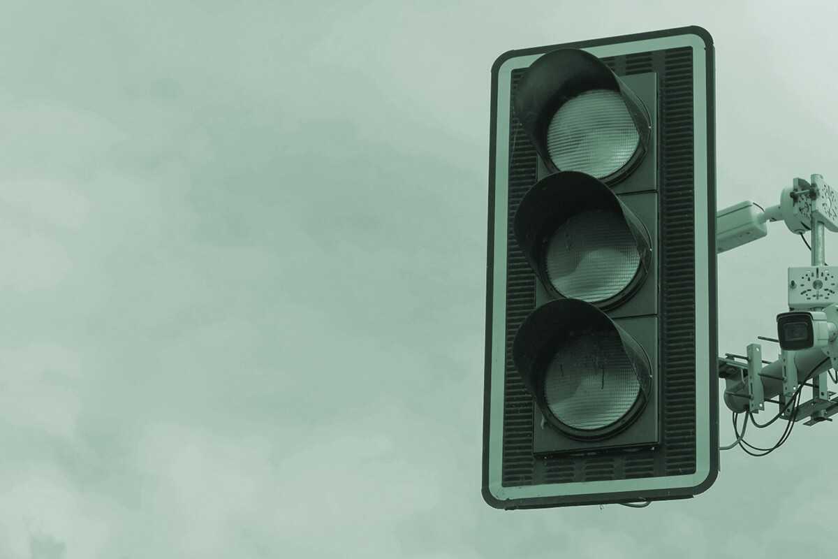 Traffic light with cameras against cloudy sky background.